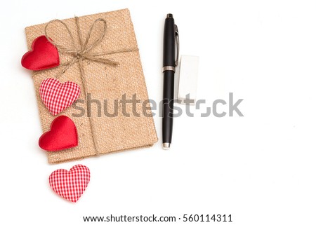 Couple of red and pink stripe heart shard put over vintage notebook beside pen and rubber on white isolated background.