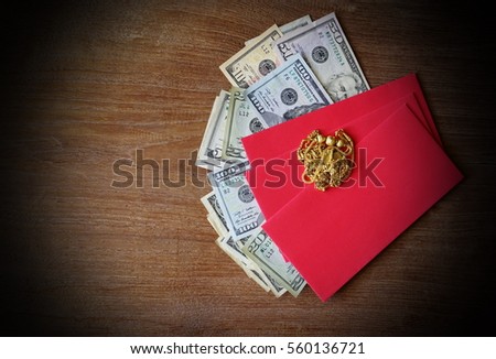 Red envelope with dollar and gold necklace for Chinese New Year bonus on wooden background.