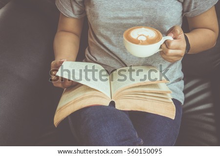 Young woman reading a book and holding cup of coffee Royalty-Free Stock Photo #560150095