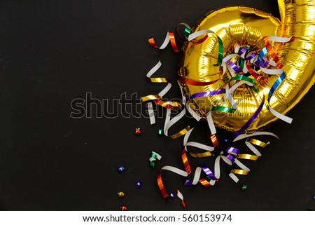 Top view of birthday party with metallic balloon and curly paper on black background
