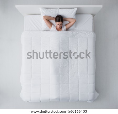 Beautiful young woman lying down in bed and sleeping, top view Royalty-Free Stock Photo #560166403