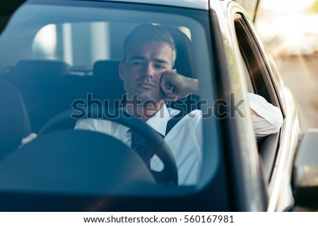Pensive disappointed businessman sitting in his car and thinking with hand on chin