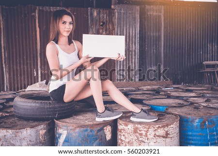 cute girl holding white paper on the palm sitting on oil barrels