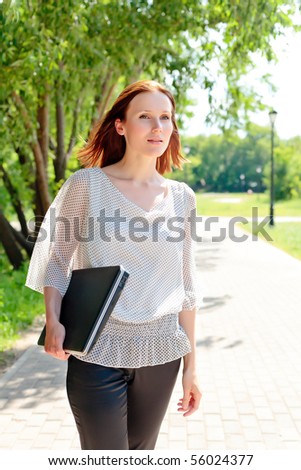 Pretty young woman walking with laptop under the hand.