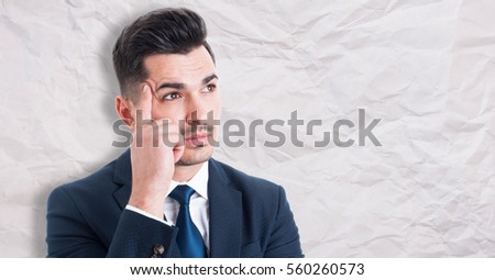 Portrait of pensive young businessman searching for successful solution isolated on wrinkled paper background with advertising area