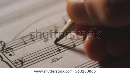 Macro close up of musician or composer hand writes a song or a musical work, writing notes with pencil on the pentagram. Concept: conservatory, music, composer, notes, art, life Royalty-Free Stock Photo #560280865