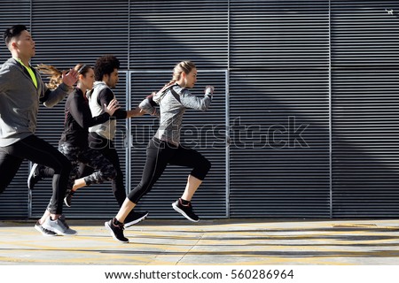 Outdoor portrait of group of friends running in the city. Royalty-Free Stock Photo #560286964