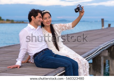 Smiling young couple making selfie while sitting on wooden bridge near the sea