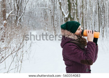 young girl drinking tea in termochashki walking in winter forest