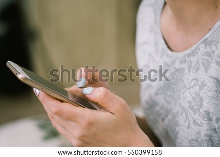 Young beautiful hipster girl with mobile phone in hands is looking in camera, while is sitting on a river jetty against blurred buildings with copy space for your advertising text message or content