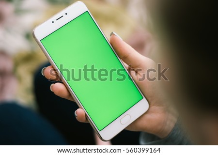 Beautiful girl holding a smartphone in the hands of a green screen green screen, hand of man holding mobile smart phone with chroma key green screen on white background, new technology concept Royalty-Free Stock Photo #560399164