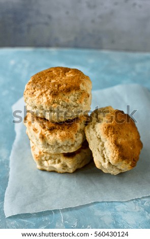 Heap of homemade English scones on a piece of parchment paper, blue and white concrete background, metallic backdrop, minimalistic rustic kitchen interior