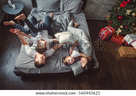 Mother, father and two sons  on the bed. Christmas. Top view of young family with two children playing on the bed  Royalty-Free Stock Photo #560443621