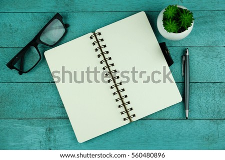 Top view of notebook, pen, eye glasses and plant on blue wooden background with copy space. 