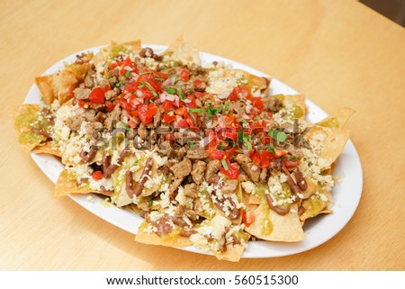 Photo of Mexican nachos with ground beef, onion, tomatoes, chili, red sauce, lettuce and lime on wooden background. Spicy and fast food concept.