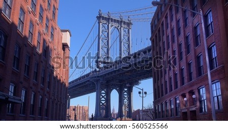 The Iconic Manhattan Bridge Viewed From Dumbo, Brooklyn, between two brick buildings with the Empire State building framed in the bottom (New York, January 2017).