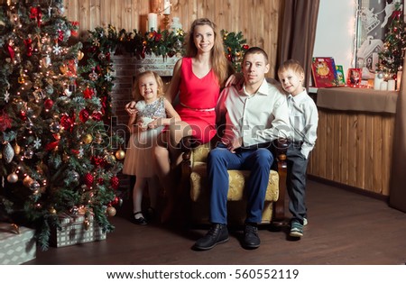 Family with children (4 years and 6 years old) dressed in red and white colors in New Year room near the fireplace and the beautiful large Christmas tree, dark browns, yellow lights