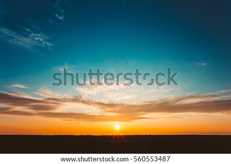 Natural Sunset Sunrise Over Field Or Meadow. Bright Dramatic Sky And Dark Ground. Countryside Landscape Under Scenic Colorful Sky At Sunset Dawn Sunrise. Sun Over Skyline, Horizon. Warm Colours. Royalty-Free Stock Photo #560553487