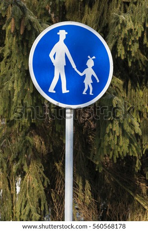 Traffic sign - pedestrian path: an adult and a girl holding hands on a background of green fir trees. Road sign used in Slovakia