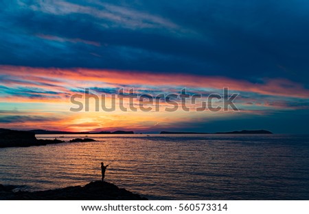 A lonely fisherman is standing on a cliff during sunset at Ibiza. When the sun is setting behind the horizon the sky is one huge set of colours.