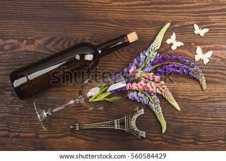 Bottle of wine and wineglass with puffy violet lupins on the wooden background