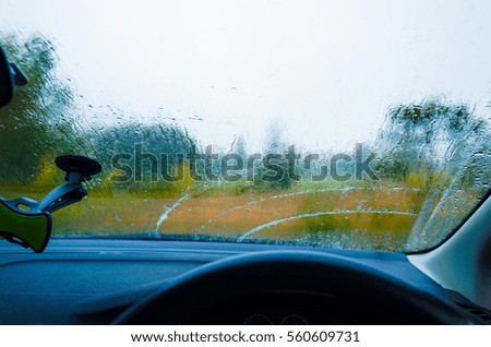 Wet car windscreen. Inside an automobile, looking out the wet window. Inside a vehicle on a rainy day, looking out through the blurry glass.