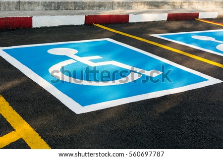 Close up of empty handicapped reserved parking space with wheelchair symbol on black asphalt. No parking white painted letters and blue diagonal lines in background. Rough cracked pavement.