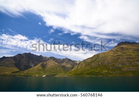 A beautiful summer landscape of lake wakatipu in Queenstown, South Island of New Zealand. Taken during a cruise where Vivid Blue sky and green hills are also seen.