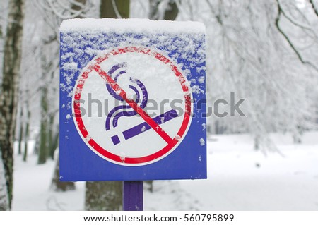 No smoking metal sign pole in the winter park. Don't smoke sign. Blue no smoking label stick to the pole in the located public park with winter background. Public park in the city for health lovers.