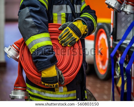 Fireman in action with a rolled fire hose on the emergency vehicle - HDR Royalty-Free Stock Photo #560803150