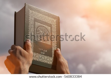 Man's hands holds Koran - holy book of muslims, on blue sky with clouds. With instagram style filter Royalty-Free Stock Photo #560833384
