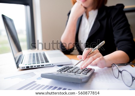 Asian female accountant or banker making calculations. Savings, finances and economy concept through a laptop. Royalty-Free Stock Photo #560877814