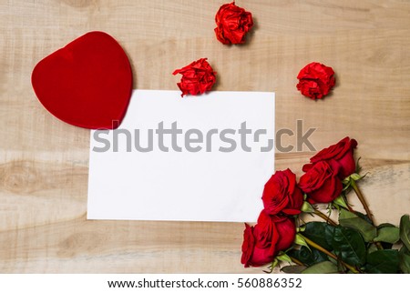 white sheet of paper, red heart, bouquet of red roses lie on a wooden table