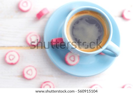 
Blue cup of coffee with candy hearts, standing on white wooden table. Sweet St. Valentine's day