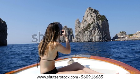 Woman taking a photo in a Boat Travel at Faraglioni Cliffs, Capri, Italy