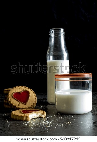 Glass and bottle of milk and biscuits on dark stone background