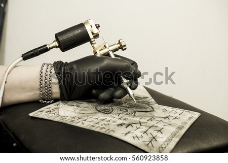 Hand of tattoo artist holding tattoo machine in process of tattooing training skin. Black gloves, concentration, art process