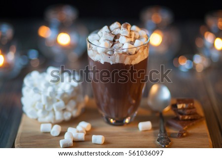 Beautiful composition - hot chocolate with marmalade and  pieces in a transparent glass. The  stands on  wooden stand. Behind the candles are burning