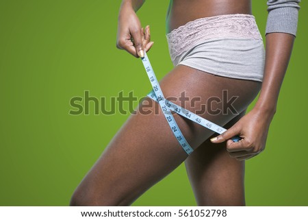 black girl is measuring her thigh with a metric tape measure