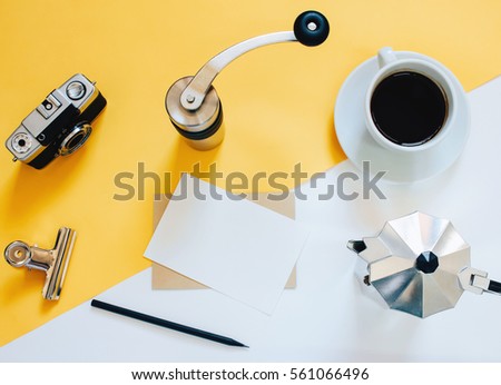 Creative flat lay photo of workspace desk with coffee maker, coffee grinder, black coffee, film camera, blank card with copy space on yellow background, minimal style