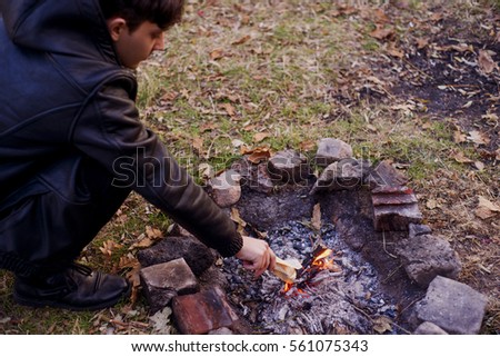 Handsome young man looking at the fire, smoldering fire, holding a book, paper, paper toss into the fire, a letter. Man dreams near the fire, the heat warms his hands. Horizontal shot.