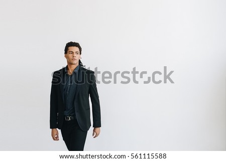 Young businessman in a black suit and blue shirt standing over white background. 