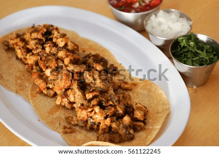 Photo of Mexican tacos with ground beef, onion, tomatoes, chili, red sauce, lettuce and lime on wooden background. Spicy and fast food concept.