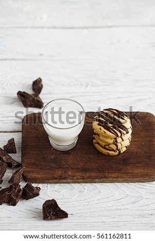 Glass of milk and stack of shortbread cookies with chocolate drizzle on a dark wooden board. White copy space. Minimal style food photography