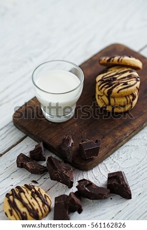 Glass of milk and shortbread butter cookies with chocolate drizzle. White wooden background. Minimalist food photography