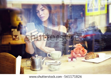 Beautiful caucasian woman with long hair texting message by mobile phone, sitting in cafe. Focus on hands. Romantic breakfast for a date or St. Valentine's Day. Present box and rose flowers. 