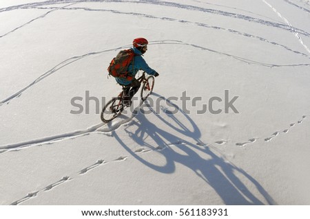Cyclist man with mountain bike rides in the fresh snow with a beautiful graphic quality shadow the joy of fresh frost and sunny Christmas morning on a frozen river. Photos from the copter