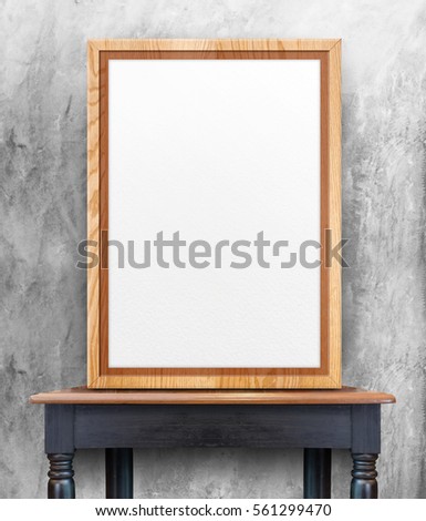 Blank wooden photo frame leaning at grey concrete wall on vintage wood table,Template Mock up for add design or text.