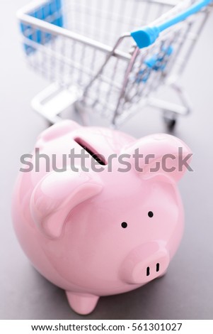 High-angle close-up view of pink piggy bank and an empty shopping cart with copy space on gray background