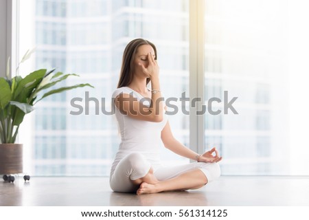 Young woman practicing yoga exercise, sitting in Sukhasana pose, Alternate Nostril Breathing technique, nadi shodhana pranayama, working out, wearing white sportswear, indoor full length  Royalty-Free Stock Photo #561314125